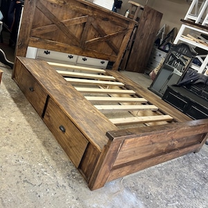 May include: A wooden bed frame with a headboard featuring a criss-cross design. The bed frame has two large drawers on the side.