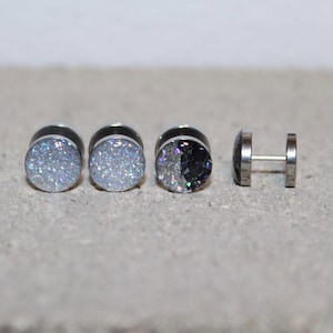 May include: Four silver-toned stud earrings. Three have a round, glittery, light blue surface. One earring has a silver post and a round, flat, silver face. The third earring has a black and silver glittery surface.