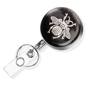 A silver-colored metal badge or lanyard with a bee design on it.