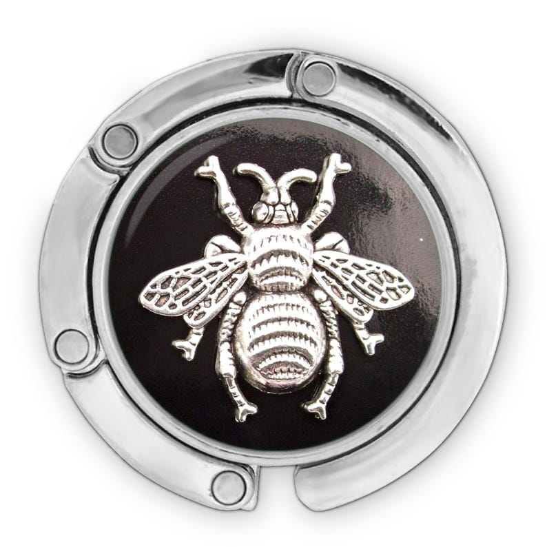 A silver-colored metal clip or hanger with a circular design featuring a detailed silver bee on it.