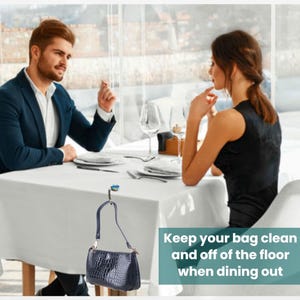 A man and a woman are seated at a table in a restaurant, engaged in conversation. The man is wearing a blue jacket, and the woman is wearing a black dress. The table is set with plates, silverware, and glasses, suggesting a formal dining setting. A handbag is hanging on the wall, and there is text in the image that reads "Keep your bag clean and off of the floor when dining out".