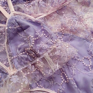 May include: Purple lace fabric with delicate floral embroidery. The fabric is soft and sheer, with a delicate texture.