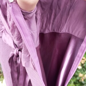 Puede incluir: Un vestido morado con cierre de cremallera lateral y un corchete de metal en la parte superior. La prenda incluye un cintur&oacute;n de tela a juego y un forro suave similar al sat&eacute;n visible en el interior, mostrando los detalles de confecci&oacute;n.