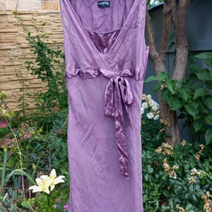 Puede incluir: Un vestido malva sin mangas con escote en V, cuerpo fruncido y un lazo de sat&eacute;n en la cintura. La prenda incluye una etiqueta que dice Long Tall Sally en el cuello interior y presenta detalles de tela texturizada en los tirantes.