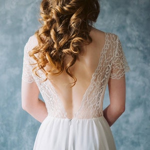 Puede incluir: Un vestido blanco de encaje con la espalda descubierta y una falda fluida. El vestido tiene mangas cortas y un corpiño ajustado.