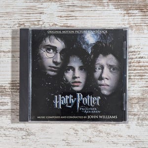 May include: A CD case featuring the Harry Potter and the Prisoner of Azkaban soundtrack. The cover art shows portraits of Harry, Hermione, and Ron. The title and composer's name are also visible.