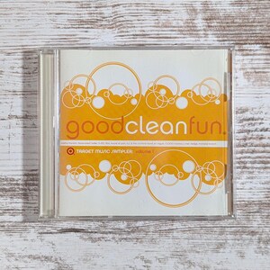 May include: A CD case with a white and orange cover. The words "goodcleanfun!" are in orange, with a bubble design. Below the title is "TARGET MUSIC SAMPLER: volume 1". The case is on a light wood surface.