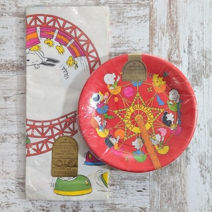 May include: Vintage Hallmark Peanuts-themed party supplies. Includes a red plate with a Ferris wheel design and "Happy Birthday" text, and a white table cover with Snoopy on a roller coaster. The table cover is 60 x 102 inches.