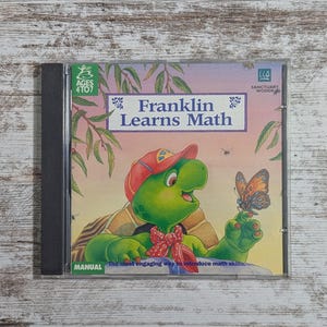 May include: A CD-ROM case featuring the title "Franklin Learns Math." The cover art depicts a green turtle wearing a red cap and bow tie, holding a butterfly. The text "Ages 4 to 7" is visible, along with the phrase "The most engaging way to introduce math skills."