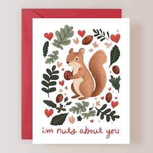 May include: Greeting card with a red envelope featuring a cartoon squirrel holding a nut. The card has a white background with illustrations of leaves, hearts, and nuts. The text "i'm nuts about you" is written in red.