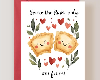 May include: A white greeting card featuring two illustrated ravioli with smiling faces, pink cheeks, and crimped edges. The text reads You're the Ravi-only one for me. The design includes small red hearts and green leaves, with a red envelope behind it.
