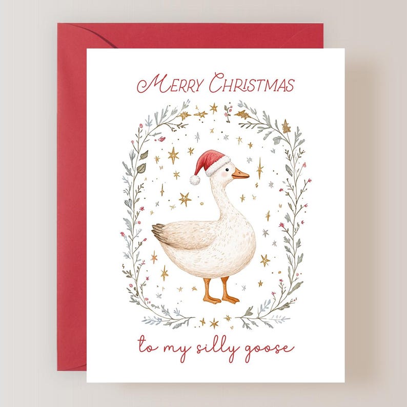 K&ouml;nnte beinhalten: Eine wei&szlig;e Gans mit einem roten Weihnachtsmann-Hut ist von einem Kranz aus blauen und gr&uuml;nen Bl&auml;ttern mit goldenen Sternen umgeben. Der Text "Frohe Weihnachten an meine dumme Gans" steht unter der Gans.