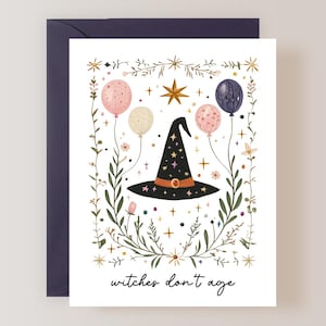 May include: A white card with a black witch's hat surrounded by green leaves, pink, white, and purple balloons, and gold stars. The text "witches don't age" is at the bottom of the card.