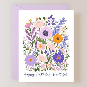 May include: A floral greeting card with a lavender envelope. The card features a colorful illustration of various flowers in shades of pink, purple, orange, and yellow. The words "happy birthday beautiful" are written in a dark blue script at the bottom.