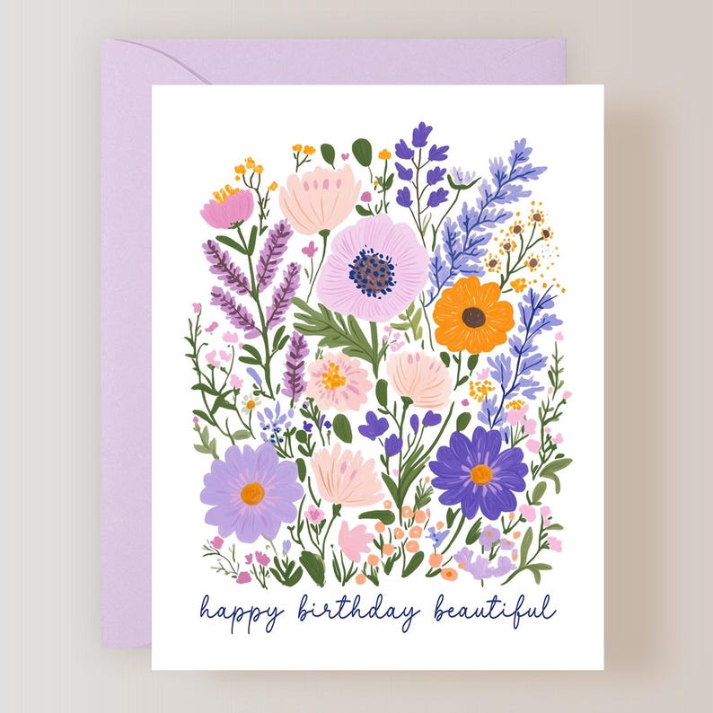 May include: A floral greeting card with a lavender envelope. The card features a colorful illustration of various flowers in shades of pink, purple, orange, and yellow. The words "happy birthday beautiful" are written in a dark blue script at the bottom.