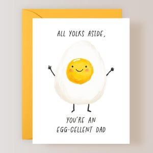 K&ouml;nnte beinhalten: Wei&szlig;e Gru&szlig;karte mit gelbem Umschlag. Die Karte zeigt ein Cartoon-Ei mit einem l&auml;chelnden gelben Eigelb, Armen und Beinen. Der Text auf der Karte lautet: &bdquo;ALL YOLKS ASIDE, YOU'RE AN EGG-CELLENT DAD.&ldquo;