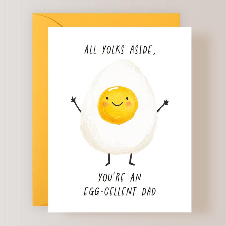K&ouml;nnte beinhalten: Wei&szlig;e Gru&szlig;karte mit gelbem Umschlag. Die Karte zeigt ein Cartoon-Ei mit einem l&auml;chelnden gelben Eigelb, Armen und Beinen. Der Text auf der Karte lautet: &bdquo;ALL YOLKS ASIDE, YOU'RE AN EGG-CELLENT DAD.&ldquo;