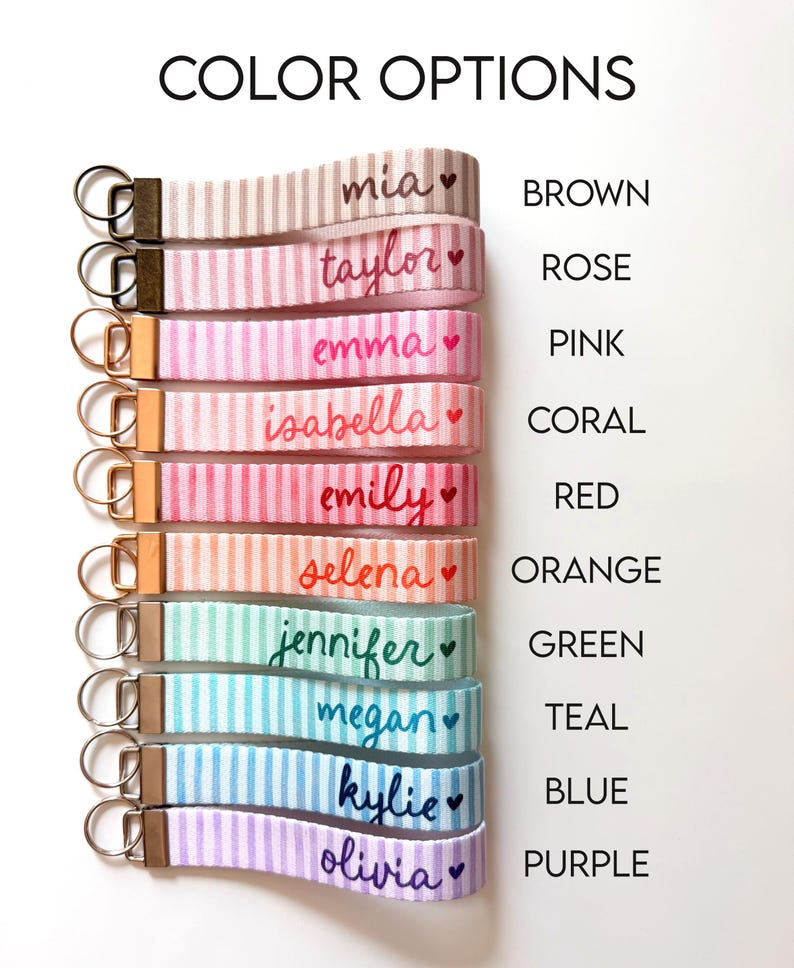 Op de afbeelding: Een selectie gestreepte pols-sleutelhangers in verschillende kleuren, elk met een naam en een hart. De kleuropties zijn bruin, roze, roze, koraal, rood, oranje, groen, blauwgroen, blauw en paars. De tekst "COLOR OPTIONS" staat bovenaan.