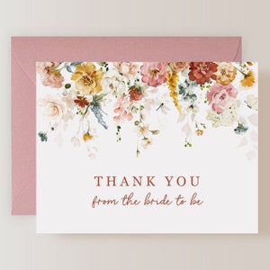 May include: A white thank you card with a floral design in shades of pink, yellow, and orange. The text "THANK YOU from the bride to be" is printed in brown.
