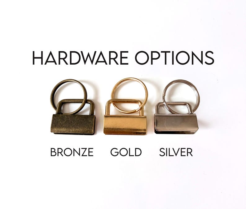 Op de afbeelding: Afbeelding van drie sleutelhanger hardware opties: brons, goud en zilver. Elke optie bevat een rechthoekige sluiting en een ronde sleutelring. De tekst "HARDWARE OPTIONS" staat boven de hardware, met de kleurnamen eronder.