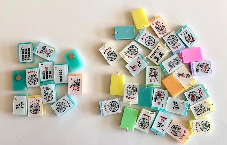 May include: A collection of colorful Mahjong tiles scattered on a white surface. The tiles feature various symbols, numbers, and Chinese characters, including "Joker" and "Win". The tiles are in shades of green, yellow, pink, and white.