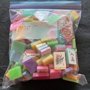 May include: A clear Ziploc bag filled with colorful Mahjong tiles. The tiles are various colors, including pink, green, yellow, and purple. Some tiles have Chinese characters and numbers.