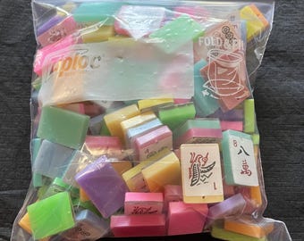 May include: A clear Ziploc bag filled with colorful Mahjong tiles. The tiles are various colors, including pink, green, yellow, and purple. Some tiles have Chinese characters and numbers.