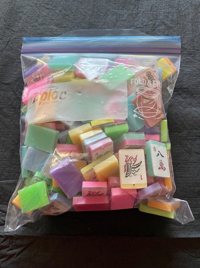 May include: A clear Ziploc bag filled with colorful Mahjong tiles. The tiles are various colors, including pink, green, yellow, and purple. Some tiles have Chinese characters and numbers.