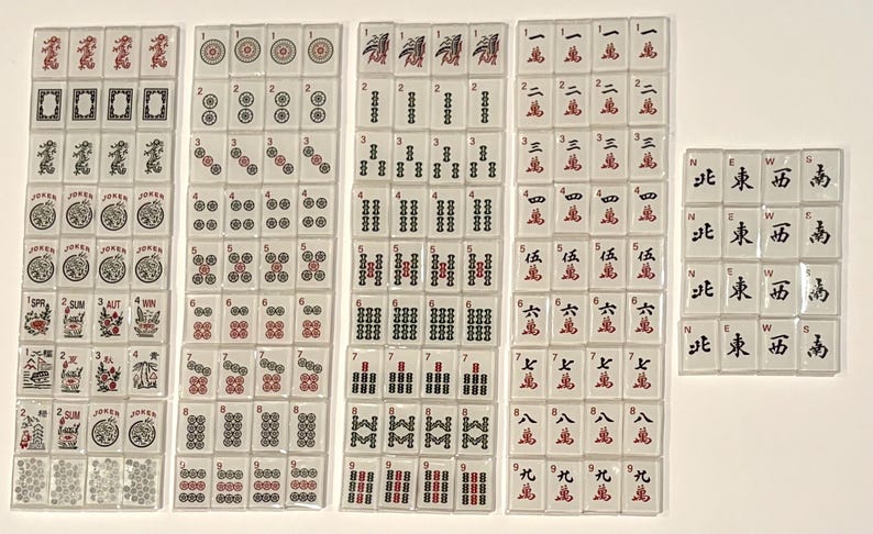 May include: A collection of white Mahjong tiles with red and black symbols and characters. The tiles are arranged in several stacks, displaying various suits, numbers, and directional markers. The set includes Jokers and flower tiles.