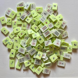 May include: A collection of light green Mahjong tiles with various symbols, numbers, and panda bear illustrations. The tiles are scattered, showing a mix of designs and colors, including red, black, and white details.