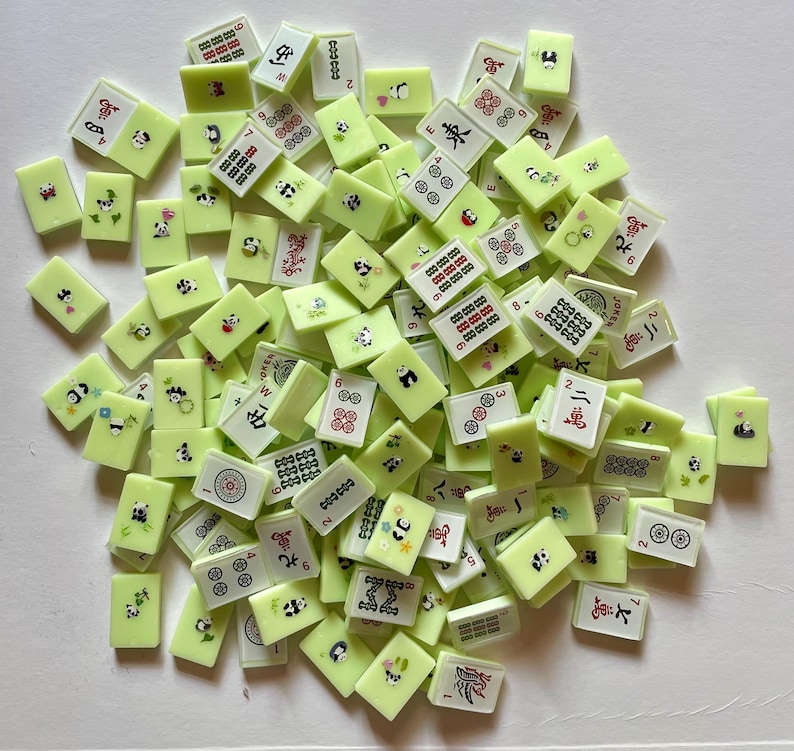 May include: A collection of light green Mahjong tiles with various symbols, numbers, and panda bear illustrations. The tiles are scattered, showing a mix of designs and colors, including red, black, and white details.