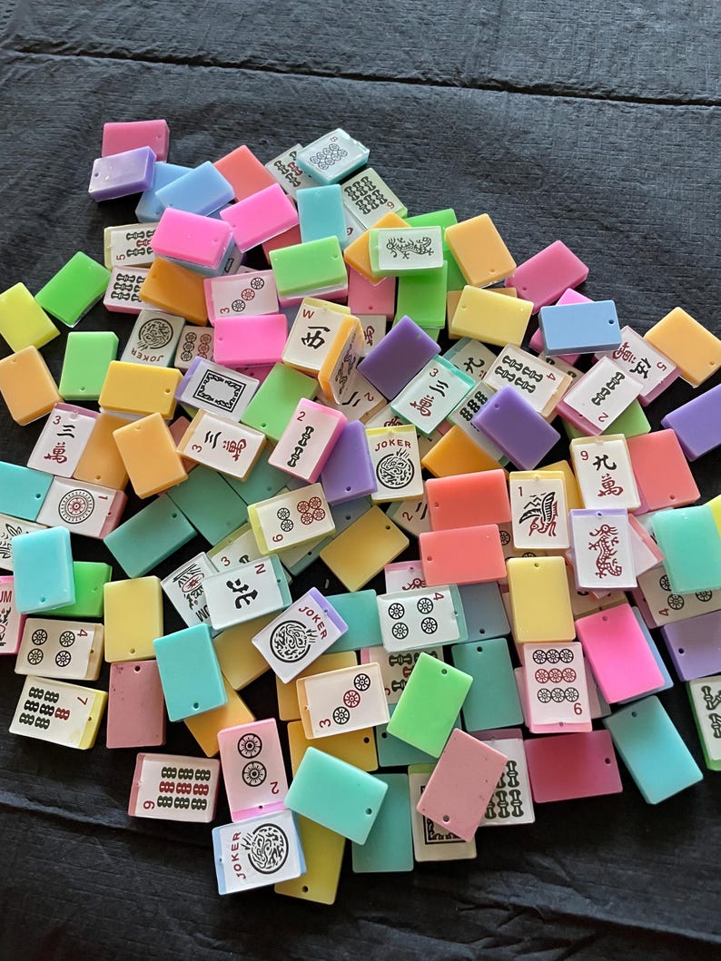 May include: A collection of colorful Mahjong tiles in various shades of pink, green, yellow, blue, and purple. The tiles feature Chinese characters and symbols, including numbers, circles, and dragons. The tiles are rectangular and made of a glossy material.