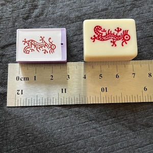 May include: Two Mahjong tiles with red dragon designs. One tile is rectangular with a purple border, the other is square and off-white. A ruler shows measurements in centimeters.