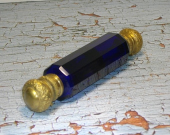 May include: A cobalt blue glass bottle with gold metal caps. The bottle is octagonal in shape and has a smooth, polished finish.