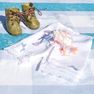 May include: A pair of olive green leather boots with brown patterned laces and a set of white fabric bloomers featuring delicate lace trim, light blue ribbon accents, and a small decorative floral embellishment with pink and yellow petals.