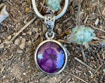 May include: A silver chain necklace with a pendant featuring a round, purple gemstone set in a silver bezel. The pendant has intricate silver detailing.
