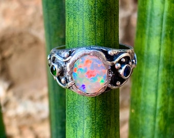May include: A silver ring featuring a large opal gemstone, surrounded by smaller green and blue gemstones.
