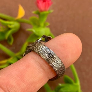 May include: A silver ring with a textured band. The ring is worn on a finger.