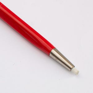 May include: A red mechanical pencil with a black tip and a silver metal tip. The pencil is angled slightly to the right against a white background. The pencil is approximately 5.5 inches long.
