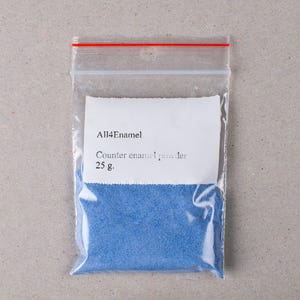 Op de afbeelding: Een doorzichtige plastic zak met blauw emaillepoeder. De zak heeft een rode ritssluiting en een wit etiket met de tekst "All4Enamel" en "Counter enamel powder 25 g."