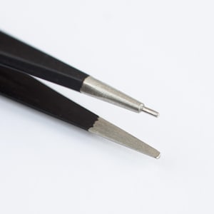 May include: Close-up of black tweezers with silver tips, designed for precision tasks. The tweezers are set against a white background, highlighting their sleek design and functionality. Ideal for crafting, beauty, or laboratory use.