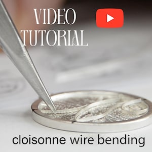 Op de afbeelding: Een close-up van een zilveren metalen schijf met een draadontwerp dat met een pincet wordt gebogen. De tekst "cloisonne wire bending" staat onder de schijf. De tekst "VIDEO TUTORIAL" staat boven de schijf met een rode play-knop.