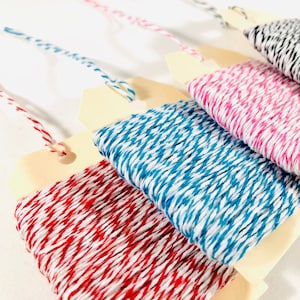May include: Four spools of twine with different colored stripes. The twine is wound around wooden spools with a white background. The colors of the twine are red and white, blue and white, pink and white, and black and white.