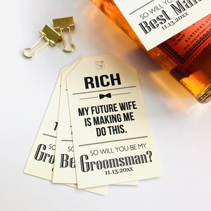 May include: A set of four cream-colored gift tags with black text. The text reads "RICH", "MY FUTURE WIFE IS MAKING ME DO THIS." and "SO WILL YOU BE MY GROOMSMAN? 11.13.20XX".