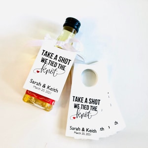 May include: White wedding favor tags with a red heart and the text "Take a shot we tied the knot" with the couple's names and wedding date.