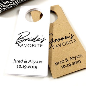 May include: Two white and brown paper bottle tags with black text. The white tag says "Bride's Favorite" and the brown tag says "Groom's Favorite". Both tags have the names "Jared & Allyson" and the date "10.19.2019".