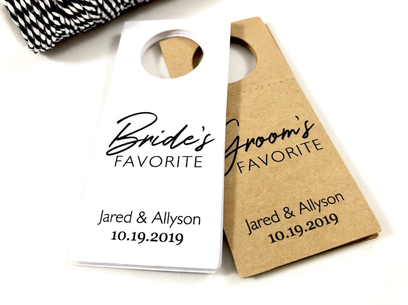 May include: Two white and brown paper bottle tags with black text. The white tag says "Bride's Favorite" and the brown tag says "Groom's Favorite". Both tags have the names "Jared & Allyson" and the date "10.19.2019".