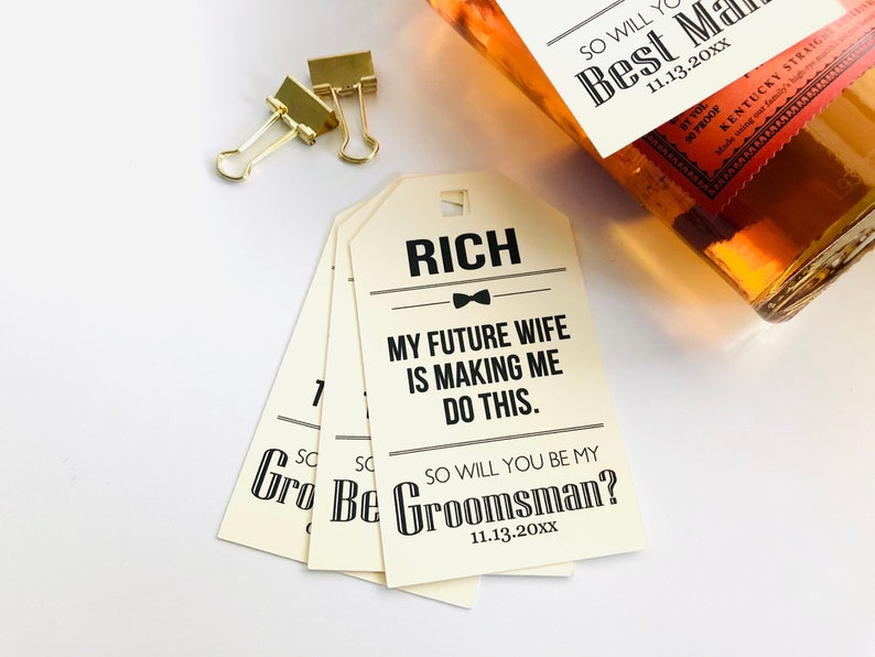 May include: A set of four cream-colored gift tags with black text. The text reads "RICH", "MY FUTURE WIFE IS MAKING ME DO THIS." and "SO WILL YOU BE MY GROOMSMAN? 11.13.20XX".