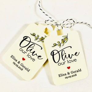May include: Two cream-colored wedding favor tags with black text that reads "Olive our love" and a small red heart. The tags also include the names "Elisa & Gerald" and the date "09.09.2018".