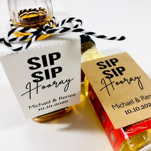 May include: Two miniature bottles of liquor with personalized labels. The labels are white and brown with black text that reads "Sip Sip Hooray" and includes the names "Michael & Renee" and the date "10.10.2020".
